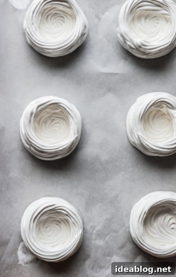 Homemade meringue cups are filled with vanilla bean whipped cream and roasted rhubarb. The perfect spring dessert! Piped Meringue Cups on Baking Sheet
