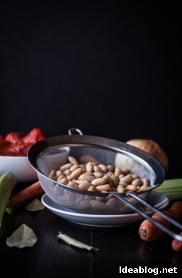 Hearty Cannellini Bolognese Spaghetti 3 Fresh ingredients for making cannellini bean bolognese, including canned white beans, diced onions, carrots, celery, and tomatoes, neatly arranged on a wooden board