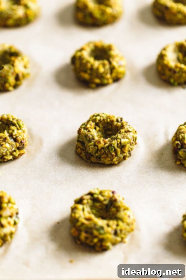 Pistachio Thumbprint Cookies with Raspberry Jam - classic thumbprint cookies are given a festive twist with homemade pistachio flour, chopped pistachios, and a raspberry jam filling! #cookies #abeautifulplate #pistachio #raspberry #thumbrpints #holidays #recipe  Unbaked thumbprint cookie dough balls with perfect indentations on a baking sheet