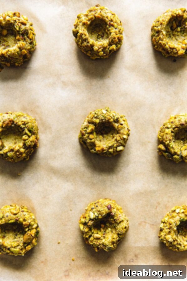 Jam-Filled Pistachio Thumbprint Cookies 7 Pistachio thumbprint cookies arranged on parchment paper before baking
