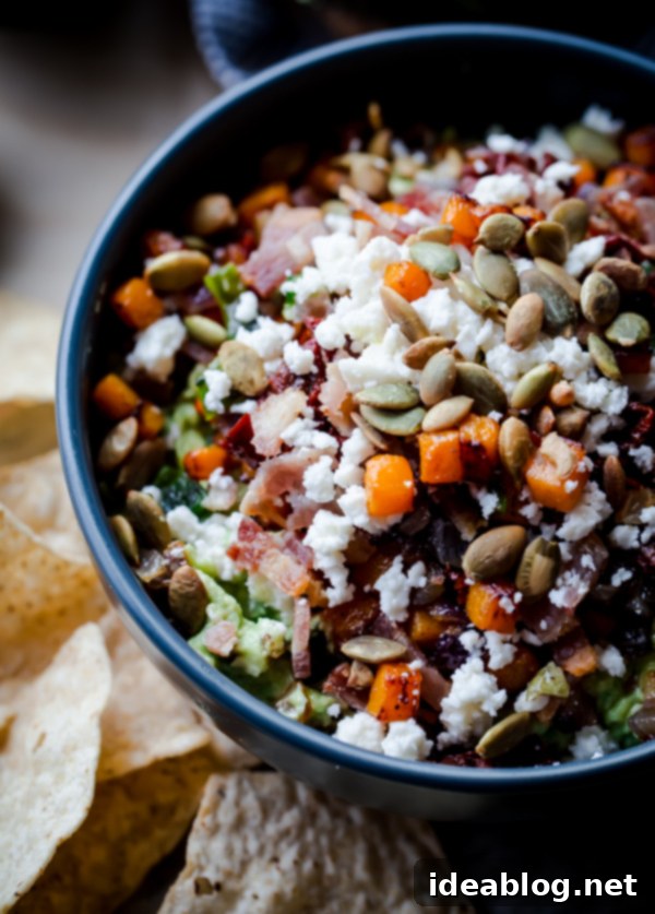 The Ultimate Guacamole 2 Delicious Fully Loaded Guacamole with tortilla chips, featuring a rich blend of toppings like crispy bacon, savory butternut squash, and sun-dried tomatoes.