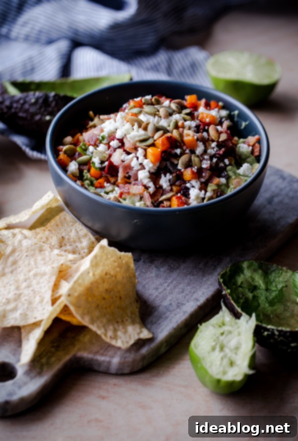 The Ultimate Guacamole 6 An overhead shot of a generous bowl of Fully Loaded Guacamole, garnished with all its components, surrounded by tortilla chips, ready for a gathering.
