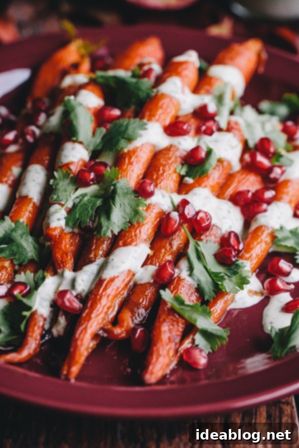 Healthy Roasted Carrot Side Dish with Tahini Roasted Carrots topped with a vibrant green tahini sauce and jeweled with pomegranate seeds