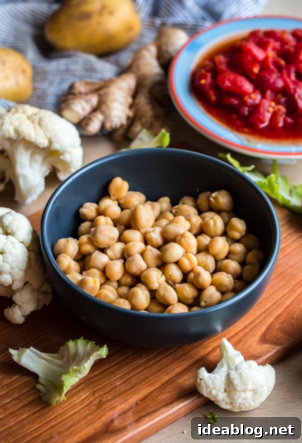 Simple Cauliflower, Potato, and Chickpea Curry Close-up of fresh ingredients for Vegan Cauliflower Curry, including cauliflower florets, potatoes, chickpeas, onions, garlic, ginger, and various spices arranged beautifully on a rustic surface.