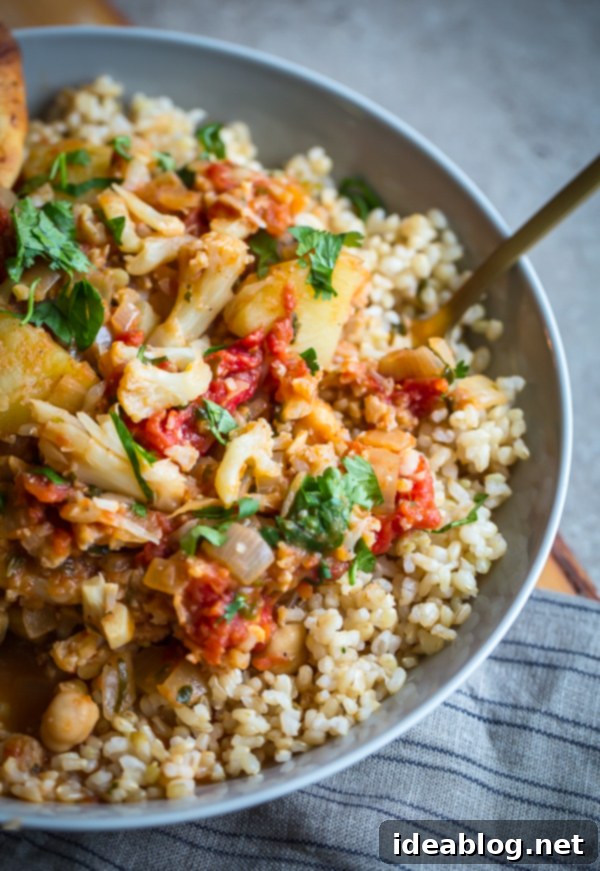 Vegan Cauliflower, Potato, and Chickpea Curry. A simple and healthy, weeknight-friendly vegan and gluten-free main course! #vegan #cauliflower #curry #potato #recipe #abeautifulplate A beautifully plated serving of Vegan Cauliflower Curry, Potato, and Chickpeas over brown rice, emphasizing its wholesome and appetizing appeal.