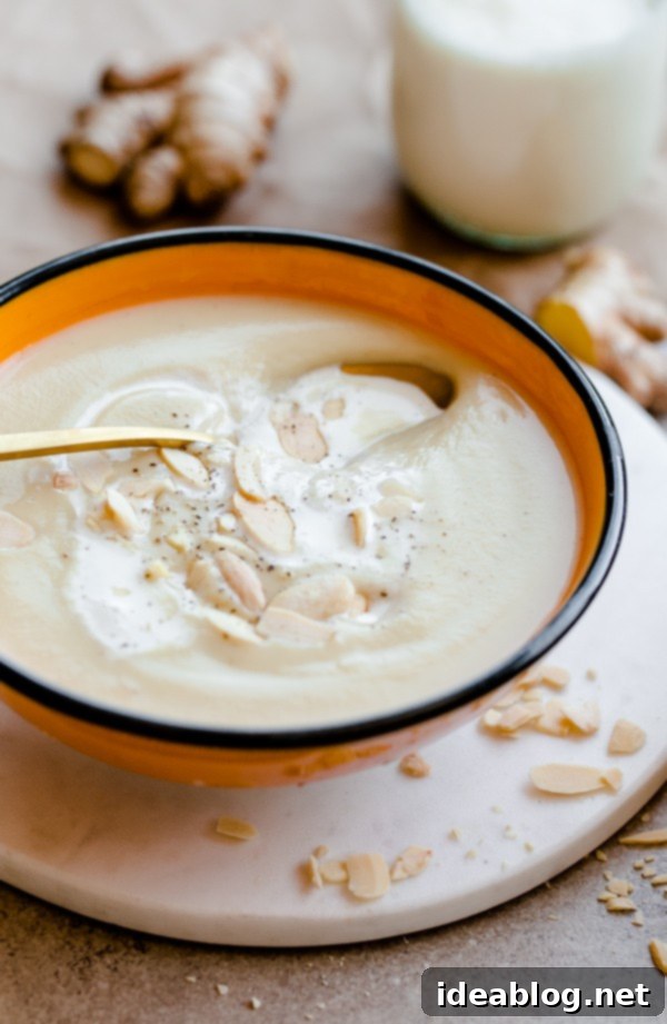 Warming Parsnip Ginger Soup 6 A bowl of creamy parsnip and ginger soup, garnished with toasted almond slices and a swirl of cream, ready to be served.