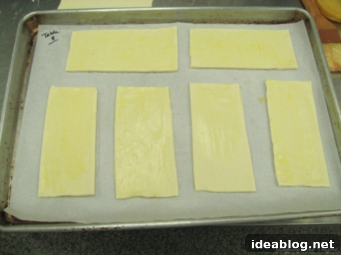 Day 16: French Bistro Delights 7 Unbaked puff pastry rectangles with Mornay sauce piped elegantly onto one half, ready for folding and baking.