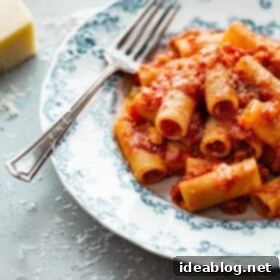 Amatriciana Pasta 11 A close-up of a serving of Pasta Amatriciana, garnished with fresh basil and grated cheese, in a rustic white bowl.