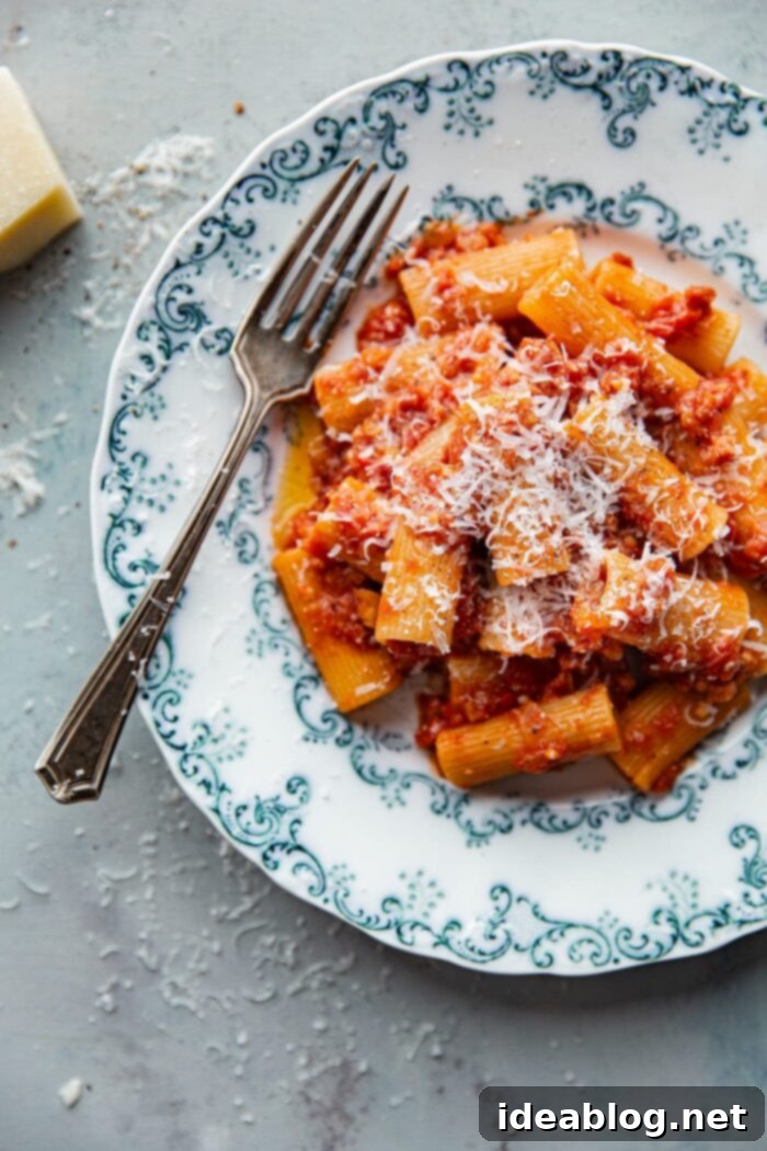 Amatriciana Pasta 3 Close-up of Rigatoni All Amatriciana, showcasing the thick, ridged pasta coated in a rich, rustic red sauce with visible pieces of crispy pancetta and a generous sprinkle of cheese.