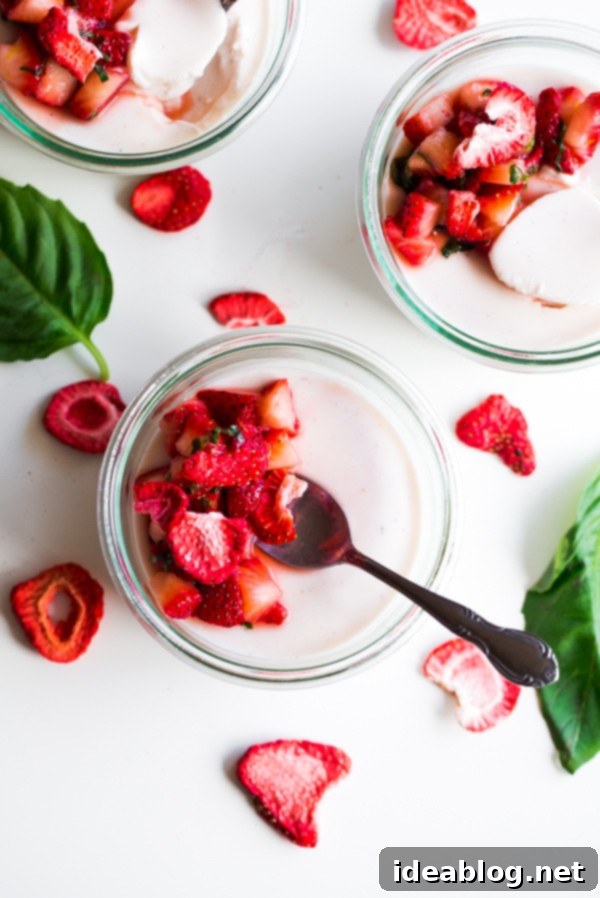 Basil-Kissed Strawberry Buttermilk Panna Cotta 4 A top-down view of a glass jar filled with Strawberry Buttermilk Panna Cotta, generously topped with macerated strawberries and fresh basil leaves.