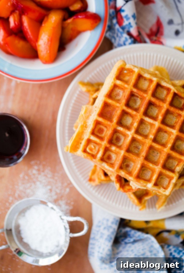 Golden Belgian Waffles with Sun-Kissed Peaches & Vanilla Cloud 5 Stack of golden Belgian Buttermilk Waffles topped with vibrant roasted peaches and a dusting of powdered sugar