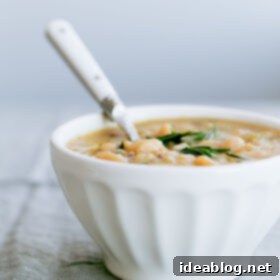 Comforting Slow Cooker Rosemary Cannellini Soup 2 A bowl of Slow Cooker Cannellini Bean Soup with Fresh Rosemary, garnished with olive oil and extra rosemary sprigs.