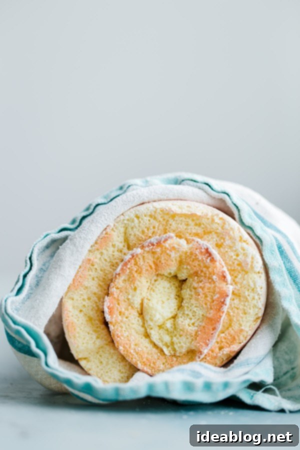 Raspberry roll cake – vanilla sponge roll cake filled with fresh raspberries, raspberry preserves, and vanilla whipped cream. This light summer cake recipe is a family favorite! #rollcake #spongecake #raspberry #abeautifulplate #recipe #dessert  Sponge Roll Cake in Kitchen Towel