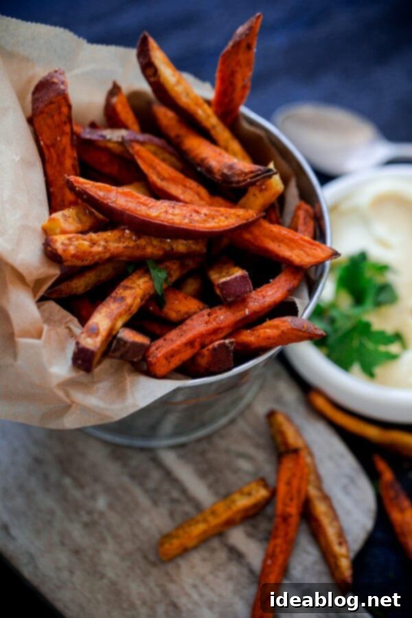 Golden Spiced Sweet Potato Fries with Creamy Garlic Aioli 7 A bowl of rich, creamy homemade garlic aioli, garnished with a sprig of fresh parsley, positioned next to a basket of crispy baked sweet potato fries.