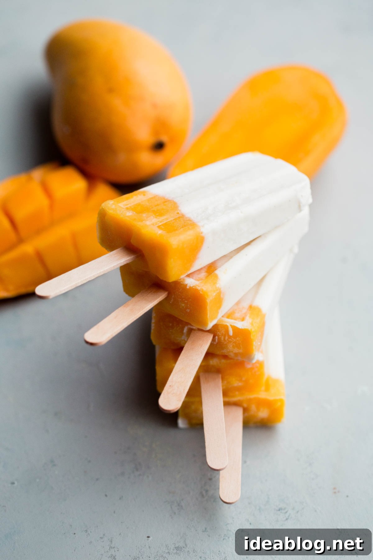 Mango Lassi Popsicles - healthy mango popsicles made with Greek yogurt, coconut milk, and fresh mango! Naturally sweetened.  Hand holding a perfectly tempered mango lassi popsicle, ready to be enjoyed on a hot day.