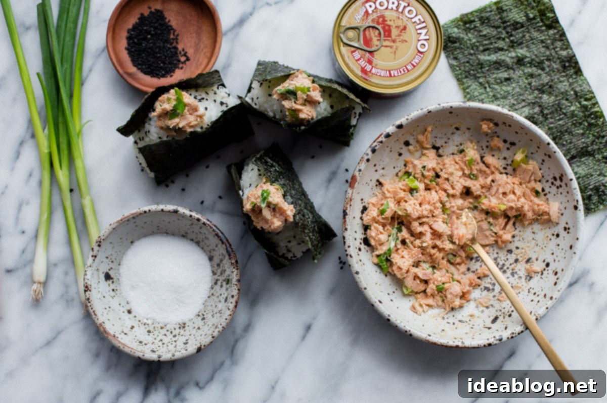 Homemade Spicy Tuna Onigiri - learn how to make homemade nigiri with this simple recipe! This spicy tuna onigiri version is filled with a simple filling of canned olive oil packed tuna, mayonnaise, sriracha, rice vinegar, and scallion. #onigiri #japanese #abeautifulplate #tuna #recipe #snack #glutenfree A close-up view of freshly prepared homemade onigiri with a visible spicy tuna filling, ready for serving.