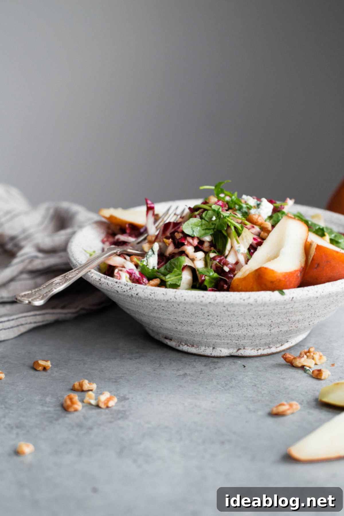 A large bowl of Fall Harvest Salad featuring mixed greens, pears, Gorgonzola, and walnuts, ready to be tossed. Bowl of Fall Harvest Salad with dressing