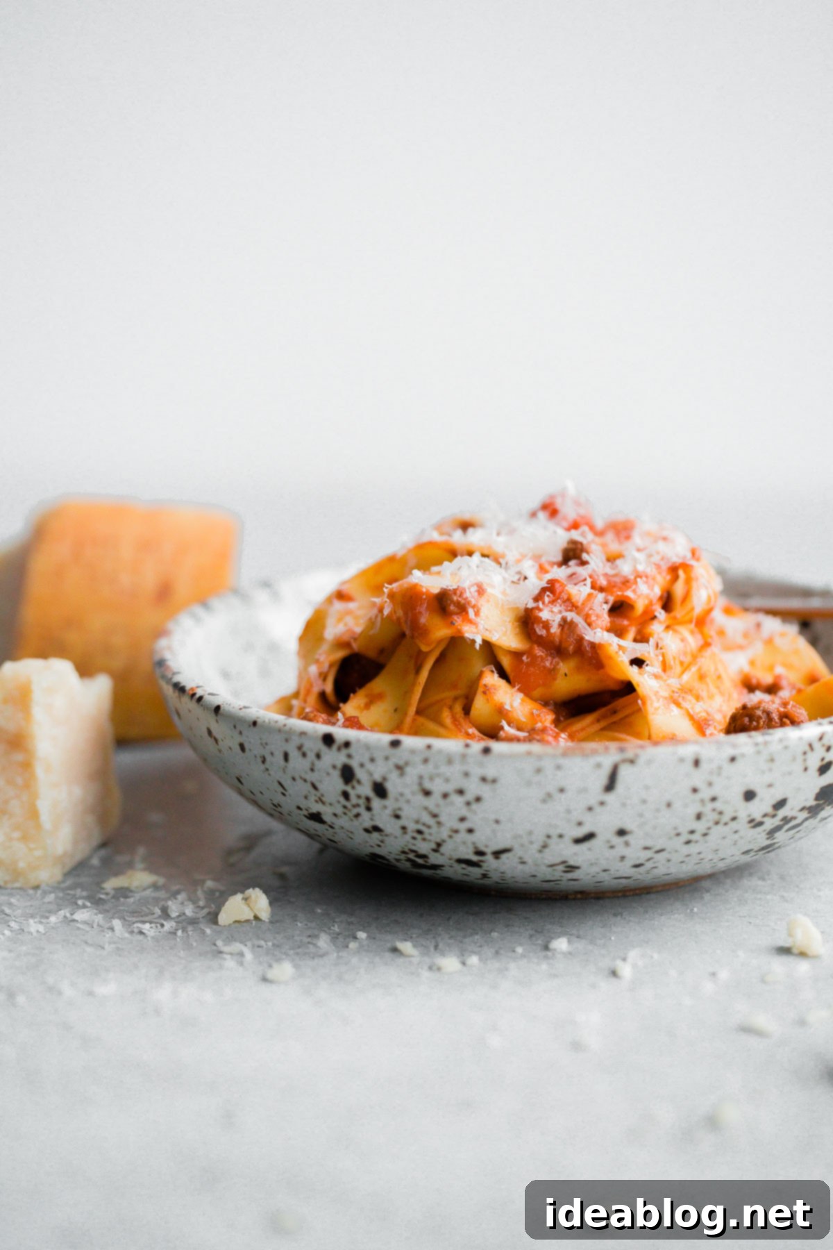 Slow Cooker Bolognese Pasta with Parmesan A close-up of slow cooker bolognese pasta in a bowl, topped with grated Parmesan cheese and fresh herbs.