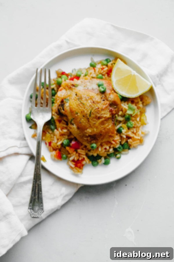 Arroz Con Pollo - an easy, comforting ONE pot meal that comes together in less than 45 minutes. This classic Spanish and Mexican dish is made with rice, chicken, bell peppers, and spices.  Arroz Con Pollo served on a white plate with fresh cilantro and lemon wedges.