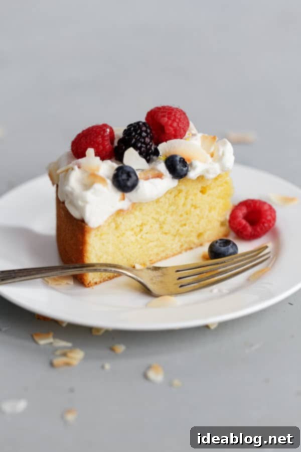 A perfect slice of Lemon Coconut Cake, showcasing its moist crumb, delicate whipped cream frosting, and fresh berry garnish. Ideal for any special occasion. #lemoncake #coconutdessert #whippedcream #freshberries #dessertlover Slice of Lemon Coconut Cake with Cream and Berries
