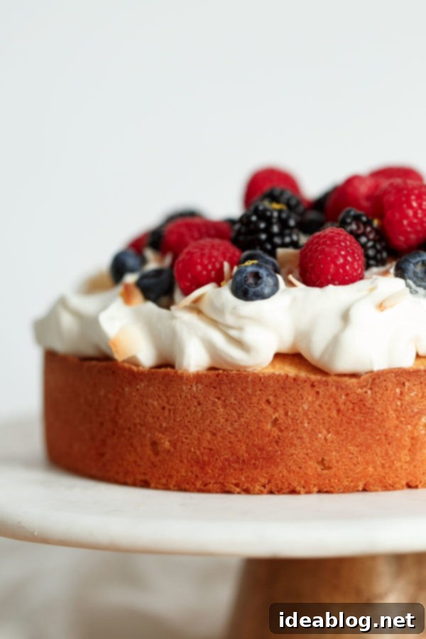 A full view of the delicious Lemon Coconut Cake, elegantly topped with whipped cream, an array of fresh berries, and toasted coconut. Perfect for any spring celebration. #lemoncoconutcake #easycake #dessertrecipe #springdessert #bobsredmill Lemon Coconut Cake with Whipped Cream and Berries