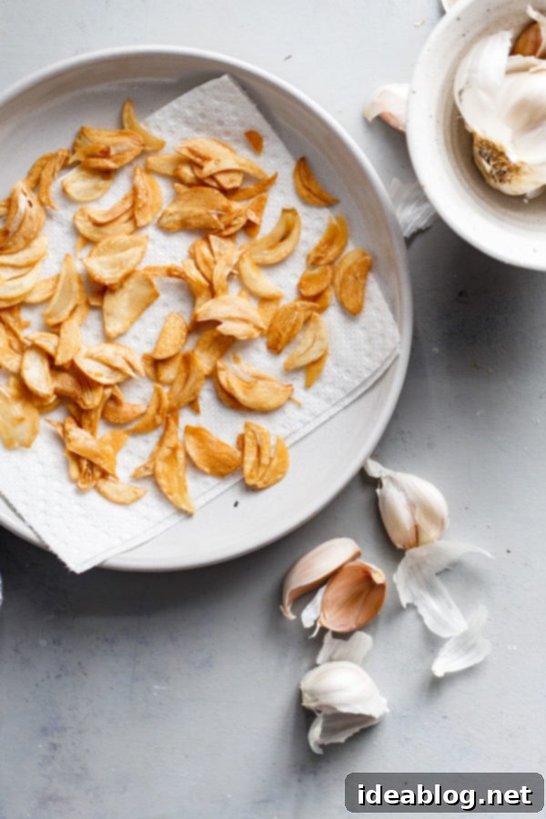 How to Make Crispy Garlic Chips - An easy, no-fuss tutorial on how to make crispy garlic chips at home, and ways to incorporate them into your cooking repertoire.  Crispy golden garlic chips artfully arranged on a clean white plate, ready to be sprinkled on any dish.