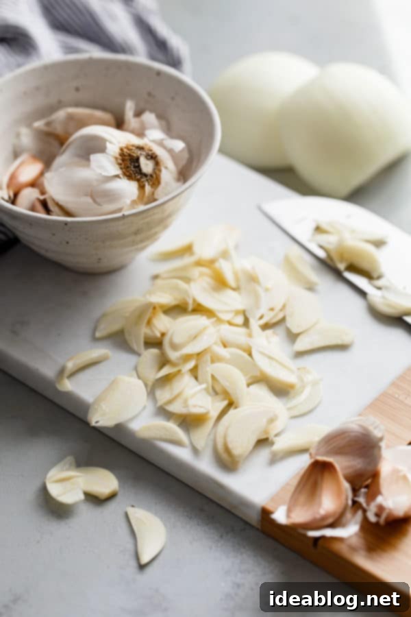 How to Make Crispy Garlic Chips - An easy, no-fuss tutorial on how to make crispy garlic chips at home, and ways to incorporate them into your cooking repertoire.  Freshly peeled garlic cloves, thinly sliced with precision, laid out on a wooden cutting board, ready for frying.