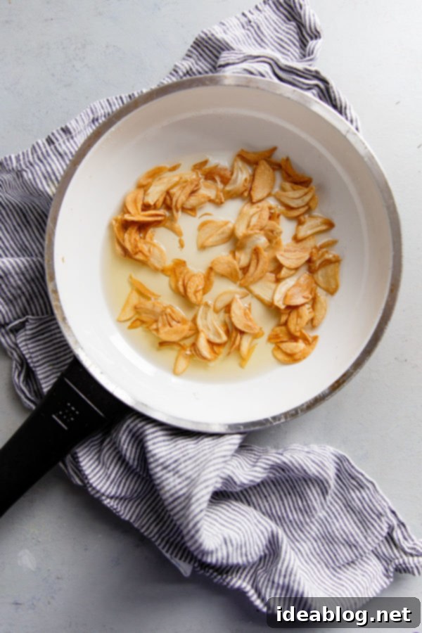 How to Make Crispy Garlic Chips - An easy, no-fuss tutorial on how to make crispy garlic chips at home, and ways to incorporate them into your cooking repertoire.  Garlic chips actively bubbling and turning golden in a small skillet filled with hot oil, illustrating the frying process.