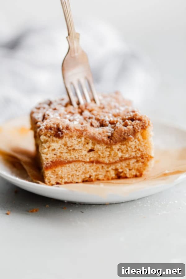 Spiced Coffee Cake with Pumpkin Butter Swirl - this AMAZING coffee cake recipe is infused with warm fall spices and filled with an incredible pumpkin butter layer. Perfect for holiday entertaining, breakfast, or brunch! Rich Spiced Coffee Cake with a visible Pumpkin Butter Swirl, garnished lightly with powdered sugar, sitting on a rustic wooden surface with fall foliage in the background, ready to be enjoyed as a perfect autumn treat.