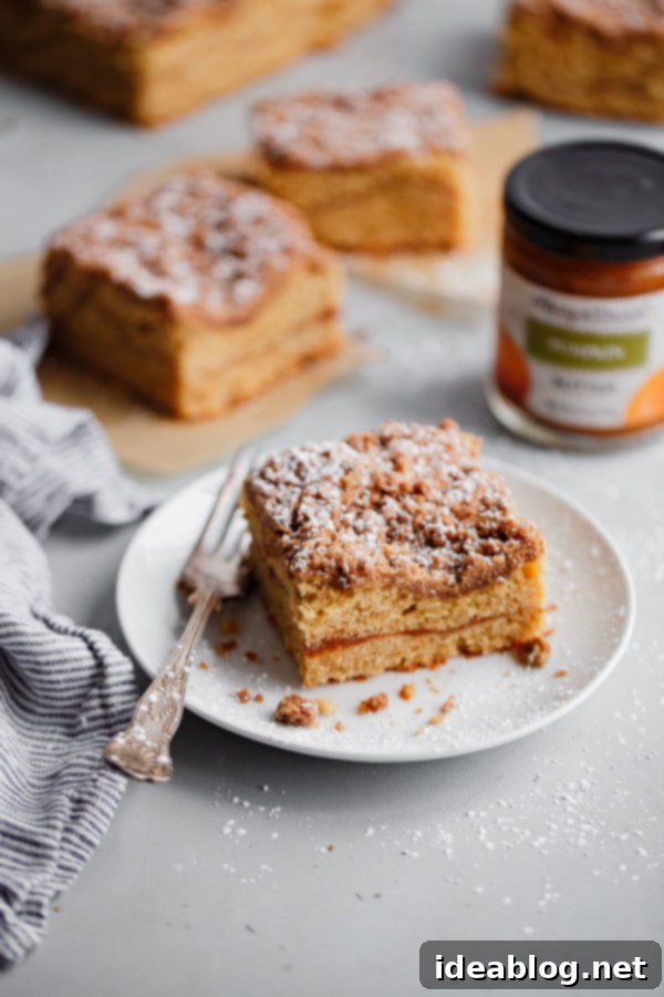 Spiced Coffee Cake with Pumpkin Butter Swirl - this AMAZING coffee cake recipe is infused with warm fall spices and filled with an incredible pumpkin butter layer. Perfect for holiday entertaining, breakfast, or brunch! Beautifully sliced pumpkin coffee cake showing the distinct orange pumpkin butter layer and crumb topping, ready to be served.