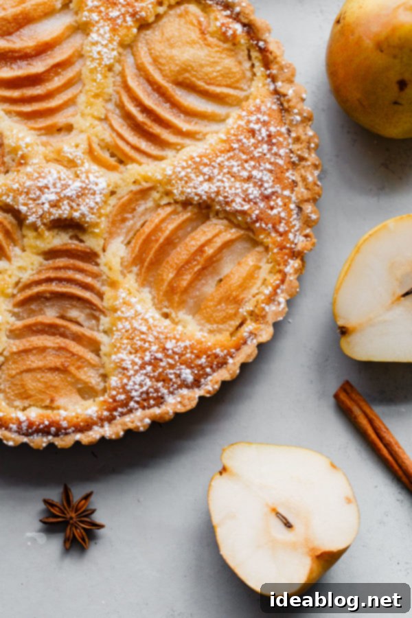 Elegant Pear & Almond Tart 4 Close-up of a Pear Frangipane Tart with a slice removed, revealing the intricate layers of crisp sweet dough, fragrant almond cream, and soft poached pears