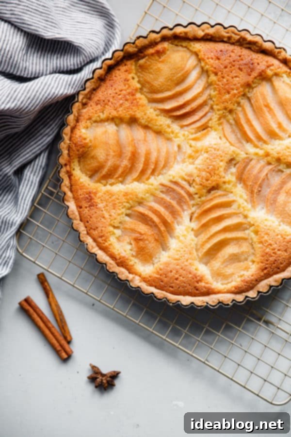 Pear Frangipane Tart - a classic French poached pear tart recipe with sweet dough, poached pears, and almond cream. Ideal for Thanksgiving or holiday season. Top with powdered sugar or apricot glaze. #tart #recipe #pear #frangipane #poached #French #dessert #pastry Elegantly arranged poached pears on a bed of frangipane filling within a baked tart shell, capturing the essence of this classic French dessert
