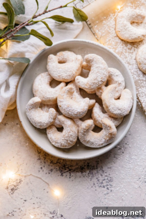 Almond Crescent Cookies - these traditional Almond Crescent Cookies (or Austrian kipferl cookies) are my go-to easy Christmas cookies. Buttery, crisp, and impossible to resist! #abeautifuplate #almondflour #kipferl #almondcrescentcookies #recipe #dessert #Christmas #holiday #baking A large pile of finished Almond Crescent Cookies, beautifully coated in powdered sugar, ready to be enjoyed.