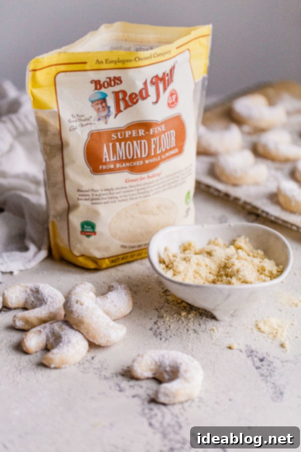 Buttery Almond Moons 2 Two almond crescent cookies on a baking sheet, showcasing their pale, delicate texture before being dusted.
