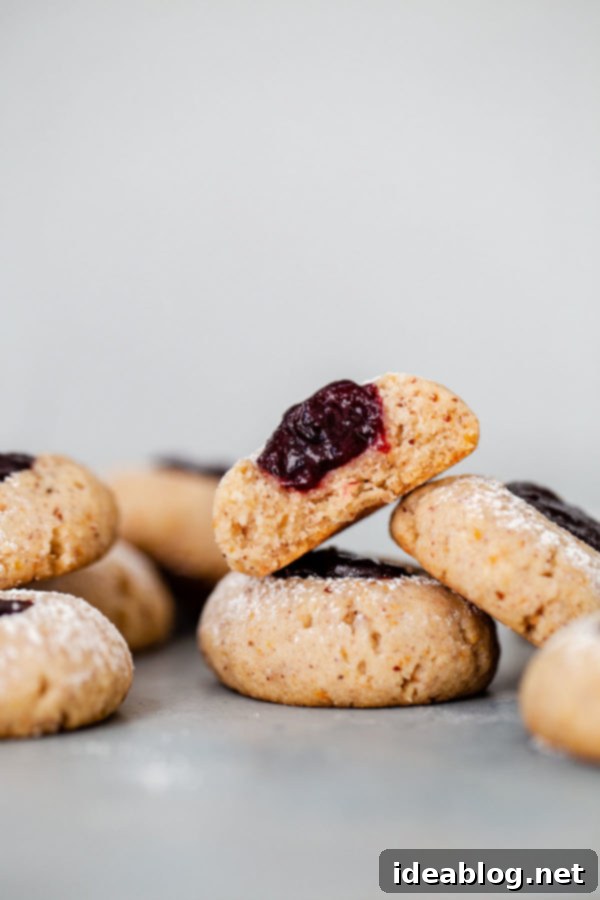 Buttery hazelnut thumbprint cookies filled with a soft berry jam center. These little cookies are easy to make, flavorful, and a lovely last-minute addition to your holiday table! #thumbprint #cookie #christmas #berry #recipe #abeautifulplate Closeup of Hazelnut Thumbprint Cookies with Fresh Jam