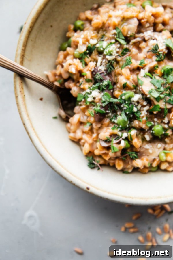 Perfectly creamy Mushroom Farro Risotto – an inviting and healthy dinner that's easy to make. A rustic ceramic bowl overflowing with rich, creamy Mushroom Farro Risotto, garnished with fresh thyme and parsley, presented on a wooden surface.