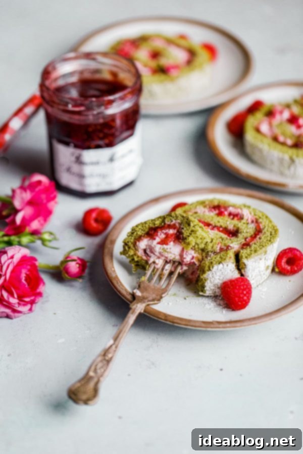 Raspberry Matcha Roll Cake - a light and elegant matcha Swiss roll filled with Bonne Maman Raspberry Preserves and a fresh raspberry cream, ideal for spring gatherings. #matchacake #raspberrydessert #swissrollrecipe Close-up of a slice of Raspberry Matcha Roll Cake, showcasing layers of green cake, raspberry preserves, and cream
