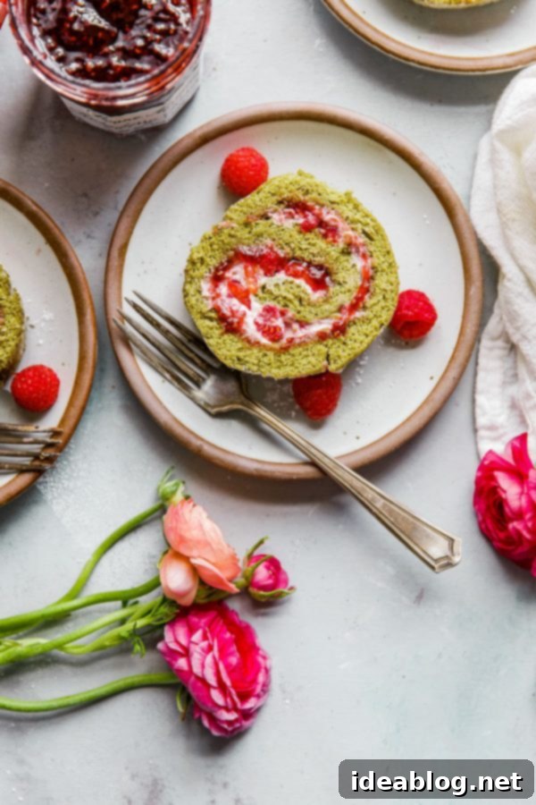 Raspberry Matcha Roll Cake with Raspberry Cream and Bonne Maman Raspberry Preserves - a delightful and elegant dessert. #matchacake #raspberrycream #bonnemamanrecipe Cross-section of Raspberry Matcha Roll Cake, showing the beautiful spiral and layers of green cake, red preserves, and white cream