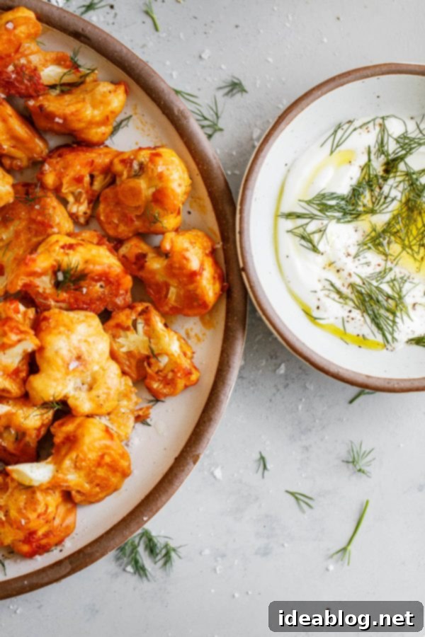 Easy Buffalo Cauliflower - these buffalo cauliflower bites are made with fresh cauliflower florets, tossed in a buttermilk flour mixture, and roasted at a hot temperature until crisp. A delicious and vegetarian twist on classic buffalo chicken! Serve with yogurt or yogurt ranch sauce. #abeautifulplate #buffalo #cauliflower #recipe #vegetarian #baked #healthy #skinny #easyrecipes Buffalo Cauliflower on Plate with Dipping Sauce