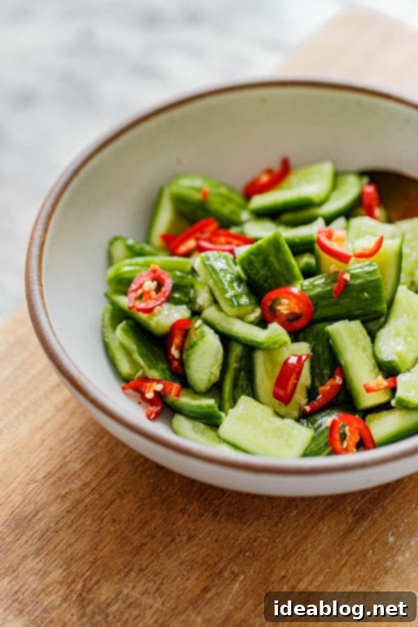 Chinese Cucumber Salad - a beautifully presented bowl of spicy, smashed cucumber salad, ready to be served. Made with sesame oil, soy sauce, rice vinegar, and chili peppers. #abeautifulplate #cucumber #salad #Chinese #recipe #glutenfree #vegetarian Chinese Cucumber Salad served in a white bowl
