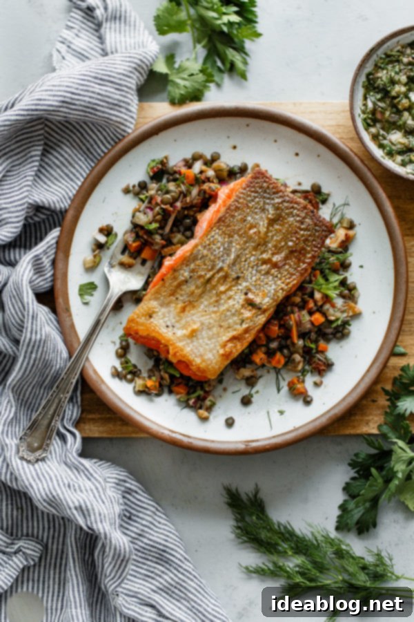 Pan Seared Salmon with Lentils - crispy pan seared salmon topped with a zesty caper herb vinaigrette and served alongside a flavorful French lentil salad. #sponsored #salmon #lentils #abeautifulplate #recipe #healthy #dinner #glutenfree #dairyfree Pan Seared Salmon with Lentils - a close-up of the final plated dish with vinaigrette.