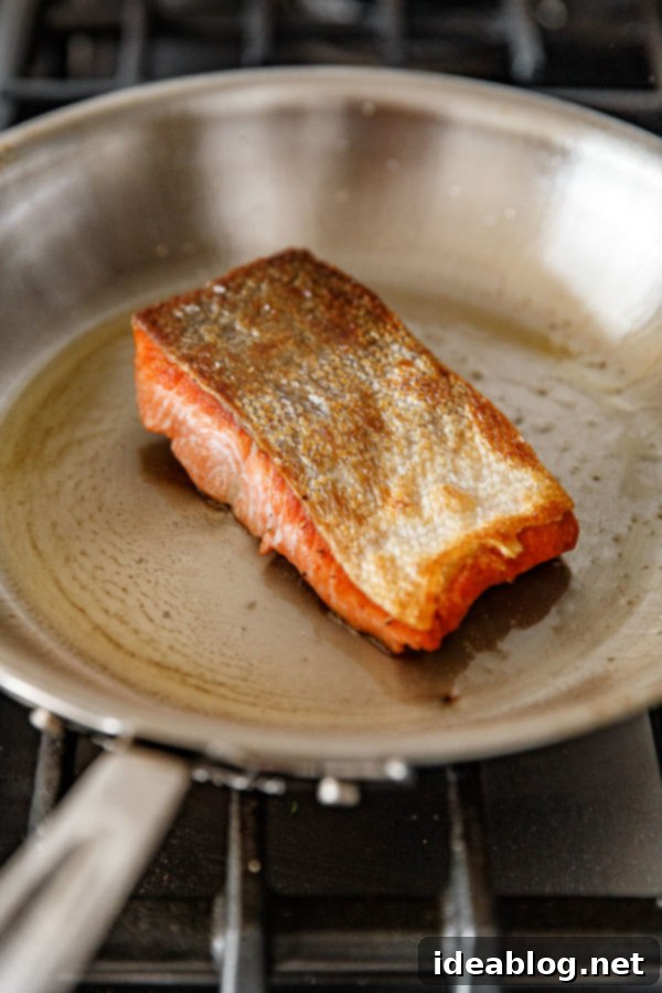 Pan Seared Salmon with Lentils - crispy pan seared salmon topped with a zesty caper herb vinaigrette and served alongside a flavorful French lentil salad. #sponsored #salmon #lentils #abeautifulplate #recipe #healthy #dinner #glutenfree #dairyfree Pan Seared Salmon in a Stainless Steel All Clad Skillet - showcasing perfect searing technique for crispy skin.