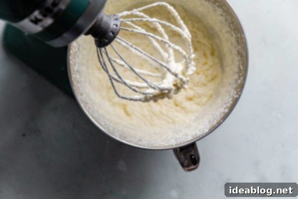 Churning Cultured Cream into Homemade Butter Stand mixer actively churning cultured cream, visibly transforming from whipped cream to separating butterfat and liquid buttermilk.