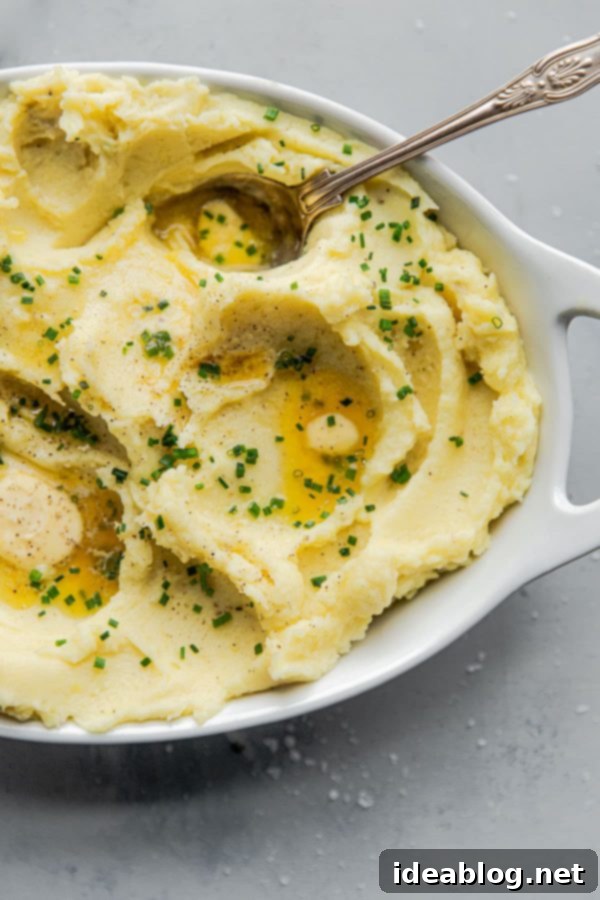 A close-up of our perfect Classic Yukon Gold Mashed Potatoes, lusciously creamy and buttery, topped with melting unsalted butter and a sprinkle of fresh chives. This simple recipe is a dream for Thanksgiving, holiday dinners, and pairs exquisitely with all your favorite main courses. #thanksgiving #holiday #potatoes #abeautifulplate #Yukongold #recipe #sidedish #easyrecipes #creamy Creamy Yukon Gold Mashed Potatoes Ready to Serve with Chives