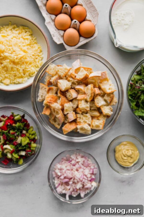 Overnight Breakfast Strata - cheesy, pillowy, and deeply satisfying, this vegetarian breakfast casserole is wonderful any time of year, but particularly ideal for holiday entertaining. #holiday #entertaining #recipe #abeautifulplate #eggs #casserole #chard #cheese #easyrecipes #vegetarian A selection of fresh ingredients laid out, including a baguette, Swiss chard, shallots, eggs, milk, and a block of cheese, ready for making strata.