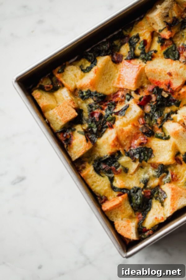 Overnight Breakfast Strata - cheesy, pillowy, and deeply satisfying, this vegetarian breakfast casserole is wonderful any time of year, but particularly ideal for holiday entertaining. #holiday #entertaining #recipe #abeautifulplate #eggs #casserole #chard #cheese #easyrecipes #vegetarian A large baking dish filled with a golden, bubbly Vegetarian Breakfast Strata, fresh out of the oven, waiting to be served.