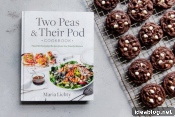 Triple Chocolate Cookies - Chewy triple chocolate cookies featuring semisweet, milk, and white chocolate chips. This chocolate cookie recipe is a chocolate lover's dream. #recipe #cookies #chocolate #abeautifulplate #desserts The 'Two Peas and Their Pod' Cookbook resting next to a plate of freshly baked chocolate chip cookies