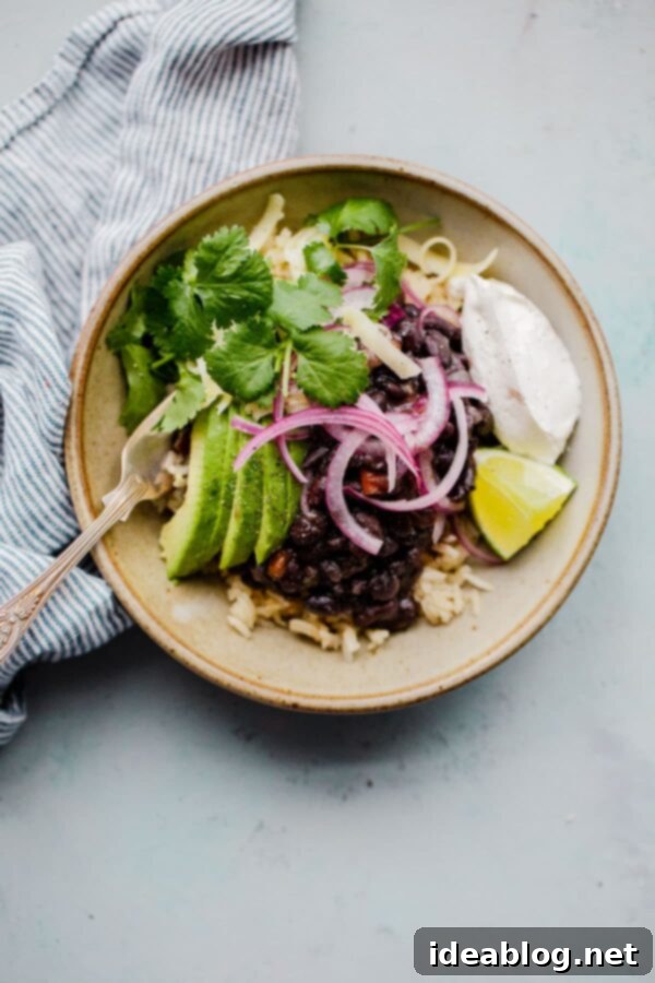 Simple Instant Pot Black Beans - pressure cooker black beans prepared with dried black beans, onion, bell pepper, and spices. These hearty, flavorful, and budget friendly black beans will quickly become a meal planning staple.  #abeautifulplate #vegetarian #blackbeans #budgetfriendlymeals #legumes #glutenfree #dairyfree #vegan A bowl of pressure cooker black beans, garnished with fresh avocado and cilantro, ready to be served.