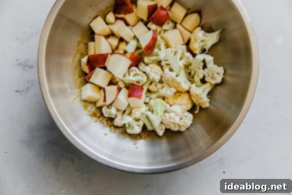 Sheet Pan Cauliflower Curry with Raita - this easy cauliflower curry, inspired by Indian Aloo Gobi, is prepared on a sheet pan and bulked up with canned chickpeas!  #vegetarian #glutenfree #curry #cauliflower #easyrecipes #sheetpan Potatoes and Cauliflower in Spice Mixture in Bowl - coated and ready for roasting