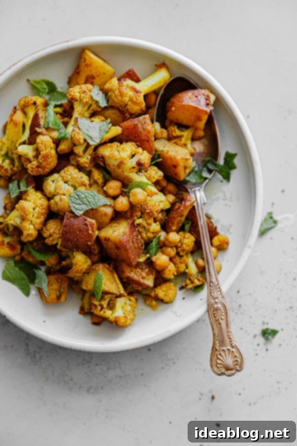 Sheet Pan Cauliflower Curry with Raita - this easy cauliflower curry, inspired by Indian Aloo Gobi, is prepared on a sheet pan and bulked up with canned chickpeas!  #vegetarian #glutenfree #curry #cauliflower #easyrecipes #sheetpan Sheet Pan Roasted Cauliflower Chickpea Curry on Platter with Serving Spoon - ready to serve
